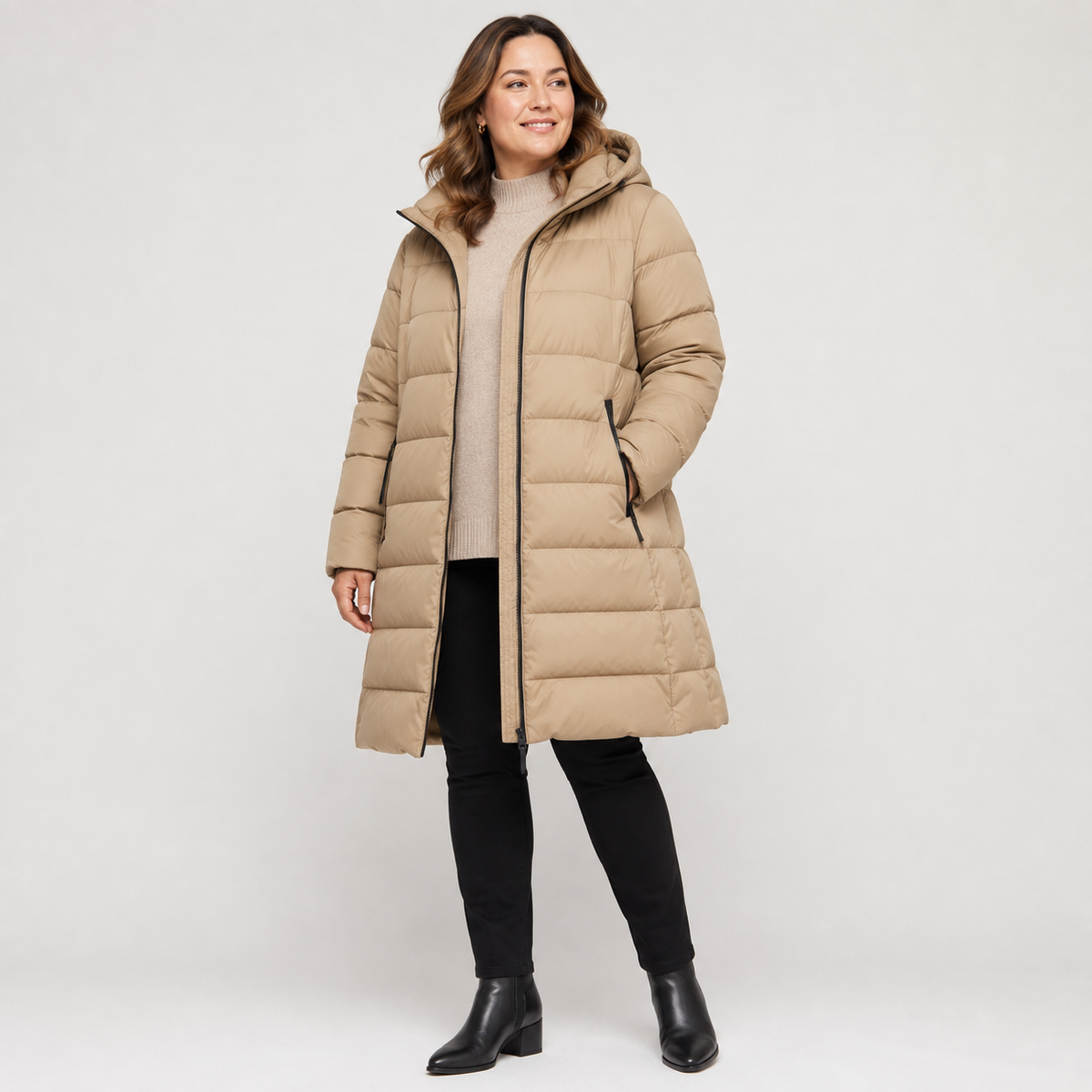 Woman wearing a beige women's mid-length hooded puffer coat in a clean studio full-body view