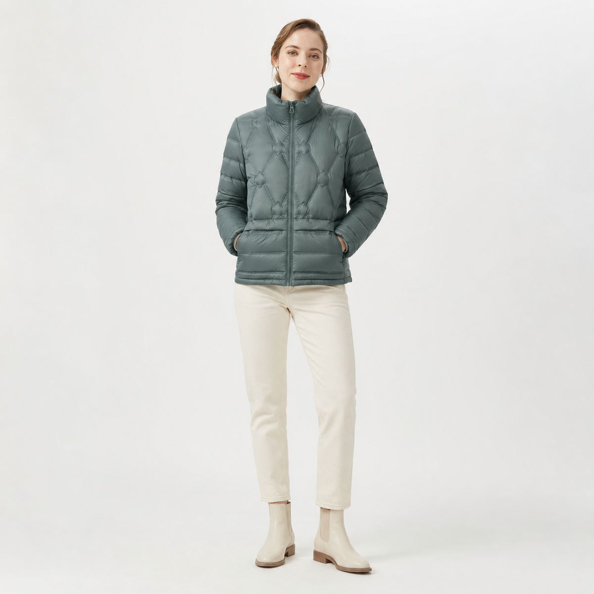 Woman wearing a sage green women's short puffer jacket in a clean studio full-body view