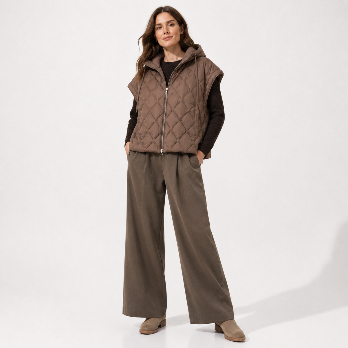 Woman wearing a taupe women's diamond-quilted hooded puffer vest in a clean studio full-body view over black top
