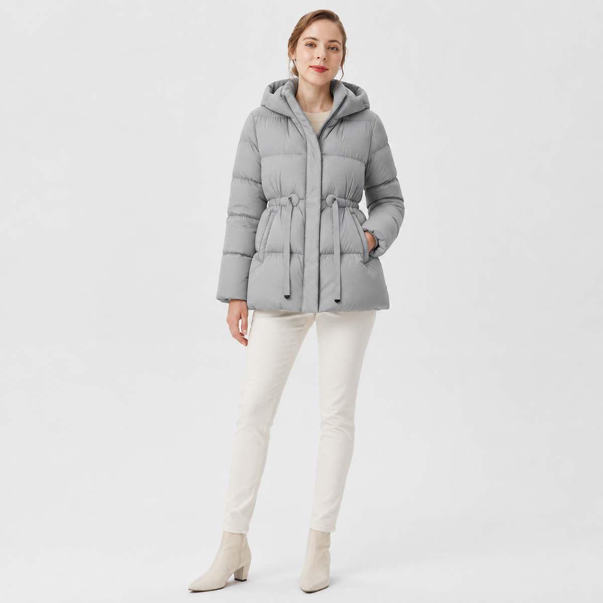 Model wearing a light gray women's hooded cinched-waist puffer jacket in a clean full-body studio view